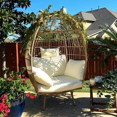 a swing chair with pillows on it sitting in the middle of a yard next to flowers