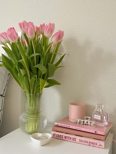 pink tulips in a glass vase on a white table next to two books