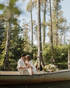 a bride and groom are sitting on a canoe in the water surrounded by tall trees