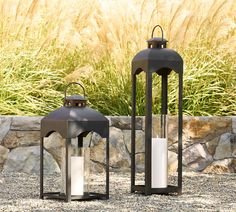 two black lanterns sitting next to each other on top of a gravel field with grass in the background