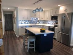 a kitchen with white cabinets and blue island in front of stainless steel refrigerator, microwave and dishwasher