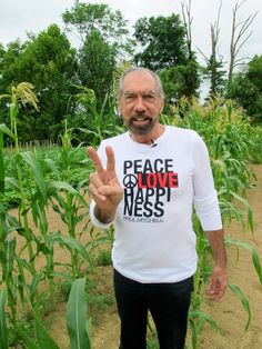 an older man standing in front of a corn field making the peace sign