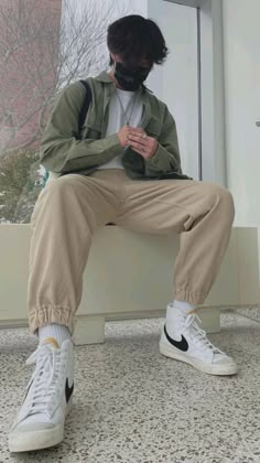 a man sitting on a window sill with his hands in his pockets and looking at his phone