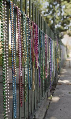 many necklaces are hanging on the side of a fence near a sidewalk and trees