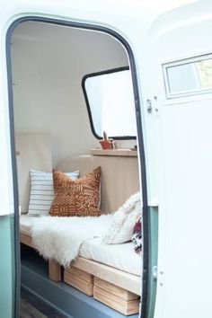 the interior of a camper van with its door open and pillows on the bed