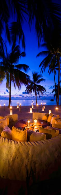 candles are lit up on the beach at night, with palm trees in the background