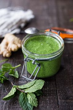 a jar filled with green liquid next to some leaves