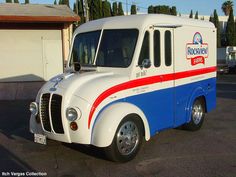 a white and blue food truck parked in a parking lot next to a garage door