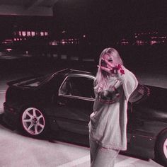 a woman standing in front of a car talking on a cell phone while holding her hand up to her mouth