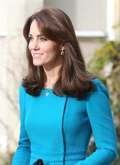 a woman with long brown hair wearing a blue dress and earrings on her cell phone