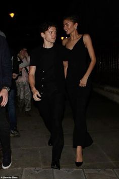 two people are walking down the sidewalk at night, one is wearing a black dress