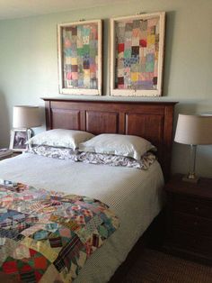 two paintings on the wall above a bed in a room with a quilt and pillows