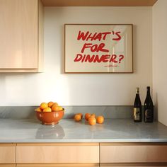 a bowl of oranges sitting on top of a kitchen counter next to bottles of wine