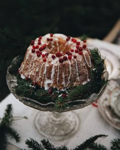 a bundt cake with white icing and cranberries on a glass plate