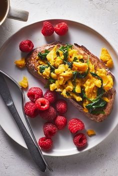 a white plate topped with toast and raspberries next to a cup of coffee