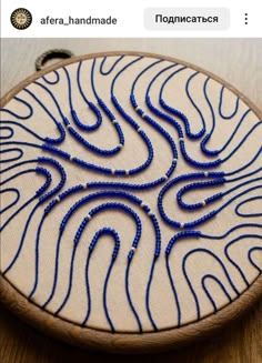 a blue beaded design is on a white piece of wood with a black thread