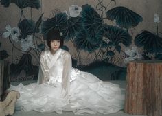 a woman in white dress sitting on the ground next to a wall with flowers and leaves