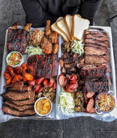 a tray with meat, vegetables and bread on it sitting on a sidewalk next to a person