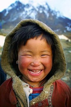 a young boy smiling and wearing a jacket with a hood over his head in the mountains