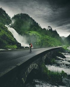 a person walking on the side of a road next to a river and mountain range