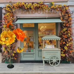 a store front with flowers on display in front of the door and behind it is a cart