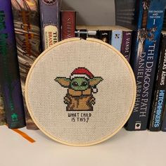 a close up of a cross stitch on a book shelf with books in the background