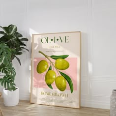 an olive poster hangs on the wall next to a potted plant in a white room