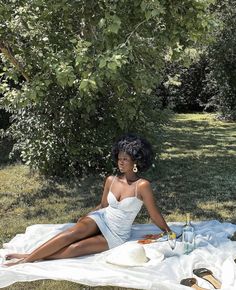 a woman sitting on top of a blanket in the grass