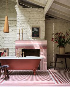 a bathroom with a pink bathtub and red striped rugs on the floor in front of a brick fireplace