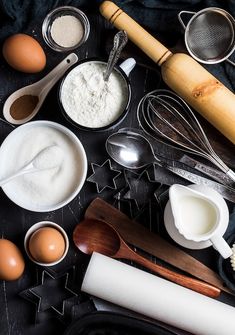 an assortment of baking ingredients on a black table with utensils and spoons