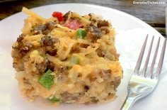 a white plate topped with a casserole covered in cheese and vegetables next to a fork