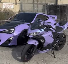 a purple motorcycle parked in front of a fence next to a black and white car