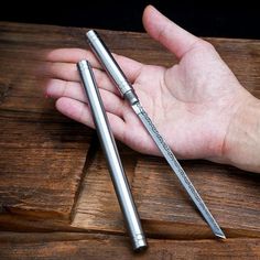 two metal pens sitting on top of a wooden table next to a person's hand