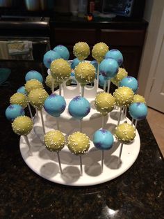 cake pops with blue and yellow frosting are arranged on a white platter in the kitchen