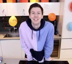 a man standing in front of a counter with balloons on the wall behind him and smiling at the camera