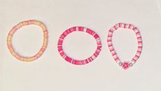 three bracelets are shown on a white surface, one is pink and the other is yellow