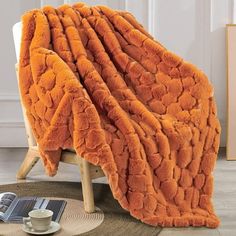 an orange blanket sitting on top of a chair next to a cup and saucer