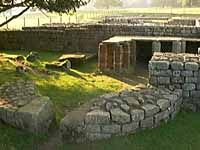 an old stone structure in the middle of a field with grass and rocks around it