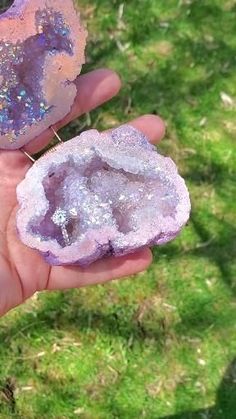 a person holding two pieces of purple and pink rock in their hand with grass behind them