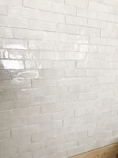 a white brick wall and wooden bench in a room with wood flooring on the side