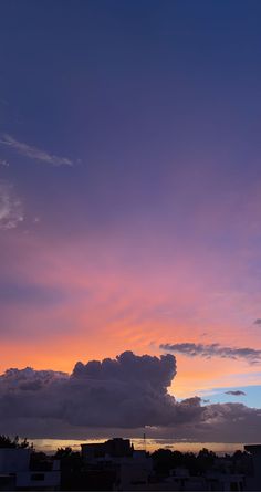 the sky is purple and orange as the sun sets over some buildings in the distance