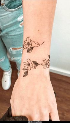 a woman's hand with a small flower tattoo on her left wrist and the other arm