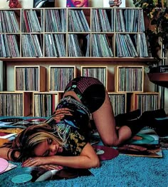 a woman laying on the floor in front of a book shelf filled with records and cds