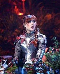 a woman with red hair wearing a silver outfit and black eyeliners on stage