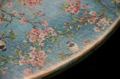 a wooden table with flowers and birds painted on the top, sitting in front of a black background