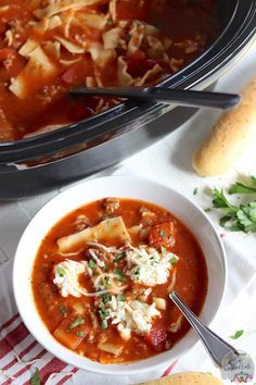 a bowl of pasta soup with bread and parmesan cheese on the side next to it