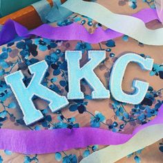 the letters k and g are made out of blue flowers on purple paper streamers