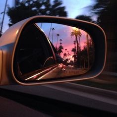 a car's rear view mirror with palm trees in the background at sunset or dawn