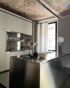 a kitchen with a metallic counter top next to a window and a painting on the ceiling