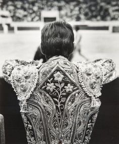 the back of a woman's head with an embroidered jacket over her shoulders at a horse show